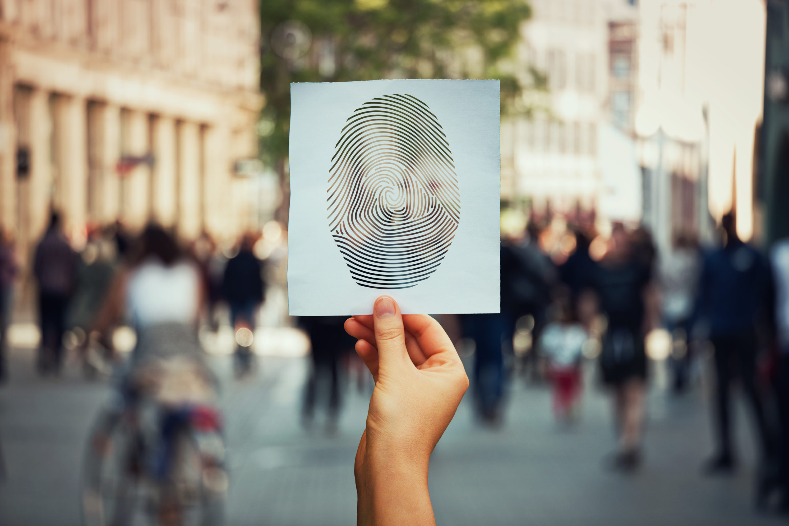 Photo of a hand holding a paper with a fingerprint on it in a crowd