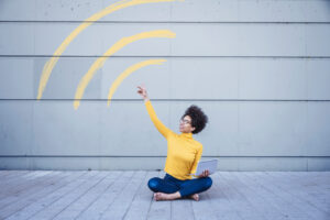 Woman sitting on ground holding laptop connected through WiFi sign