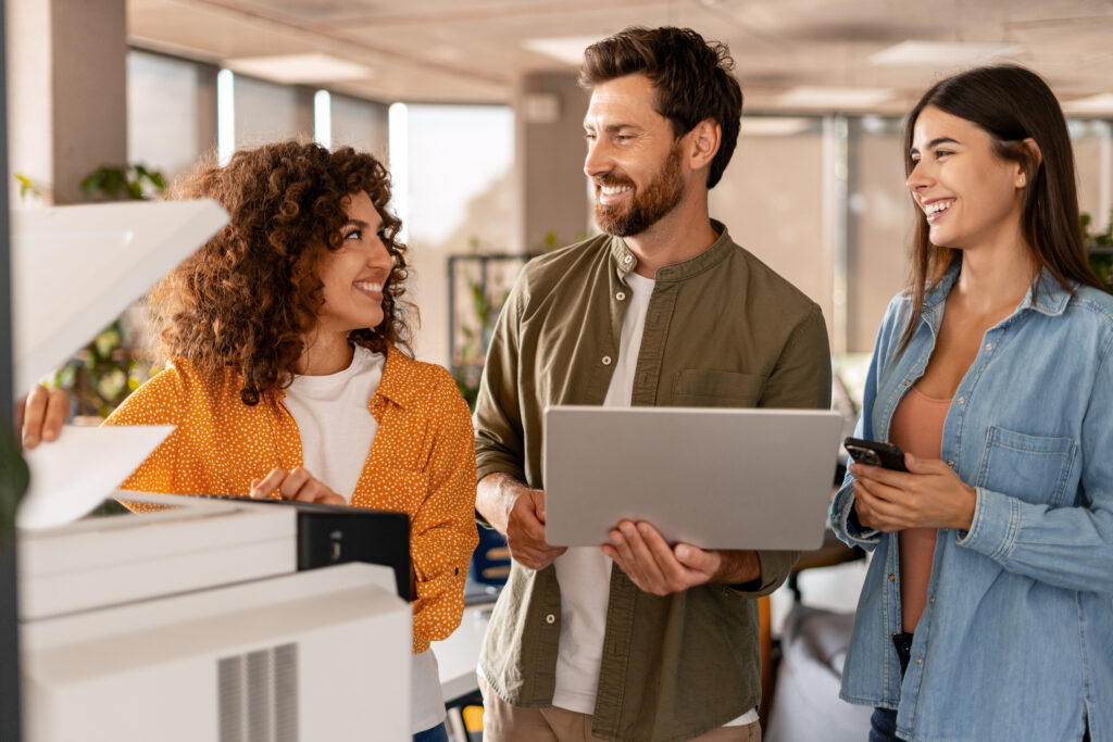 Business team printing and discussing documents in office using photocopier and laptop