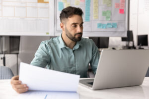 Young male entrepreneur working at desk on notebook holding papers