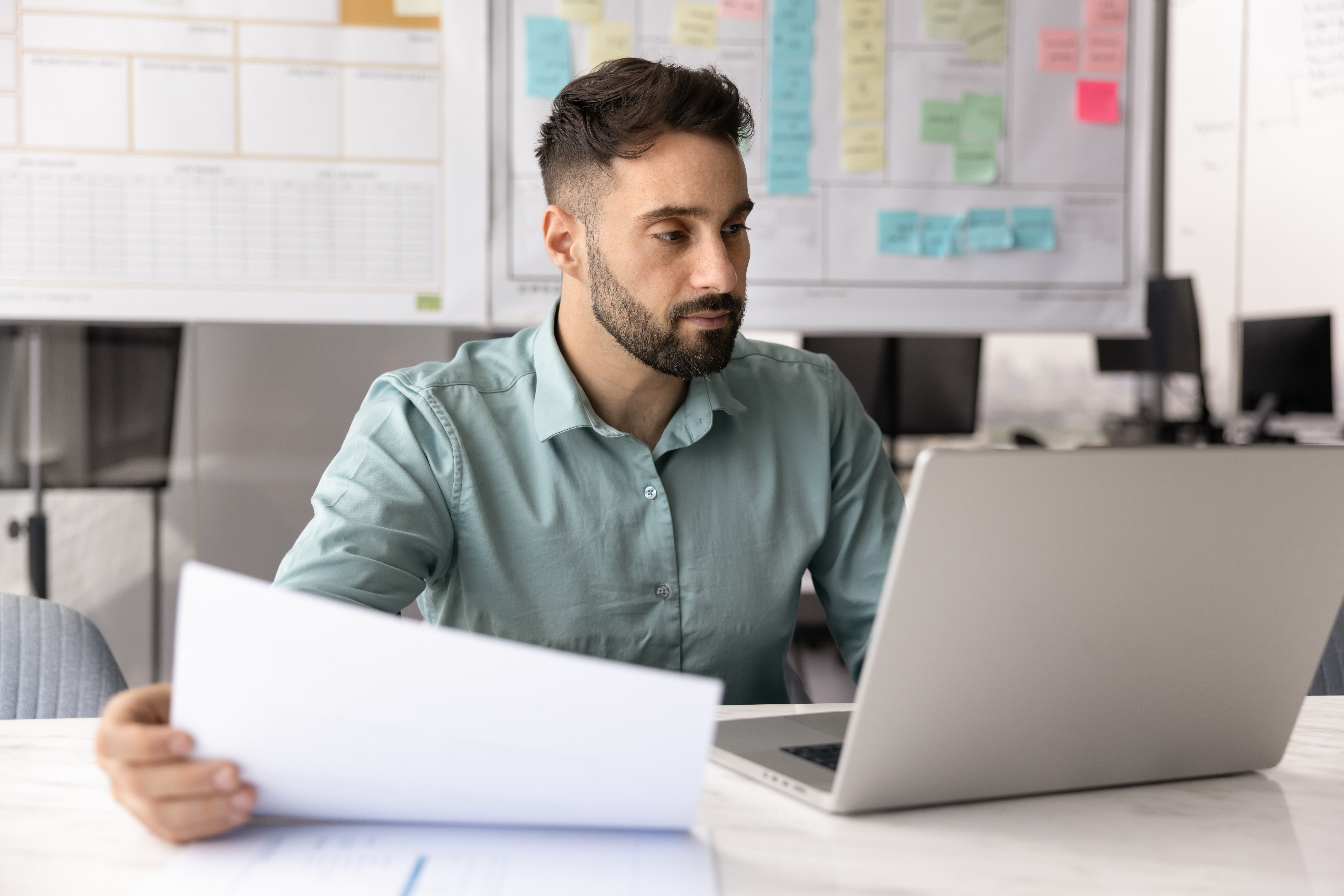 Young male entrepreneur working at desk on notebook holding papers