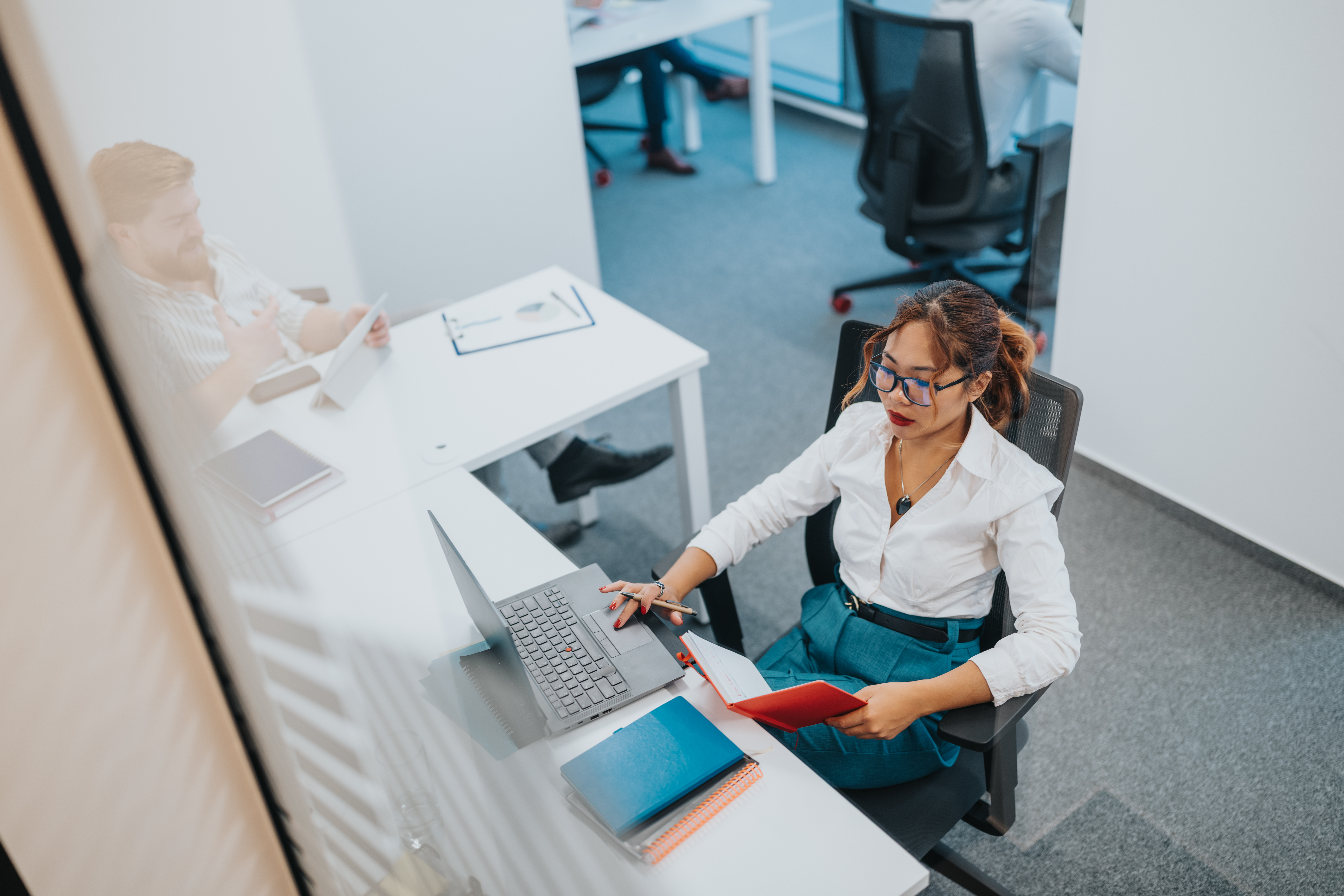 Professional woman at a desk with laptop and notebook in a modern office setting
