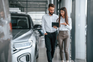 Having a business conversation. Man with woman in white clothes are in the car dealership together.