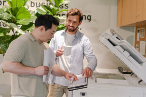Two businessmen using office printer and drinking coffee