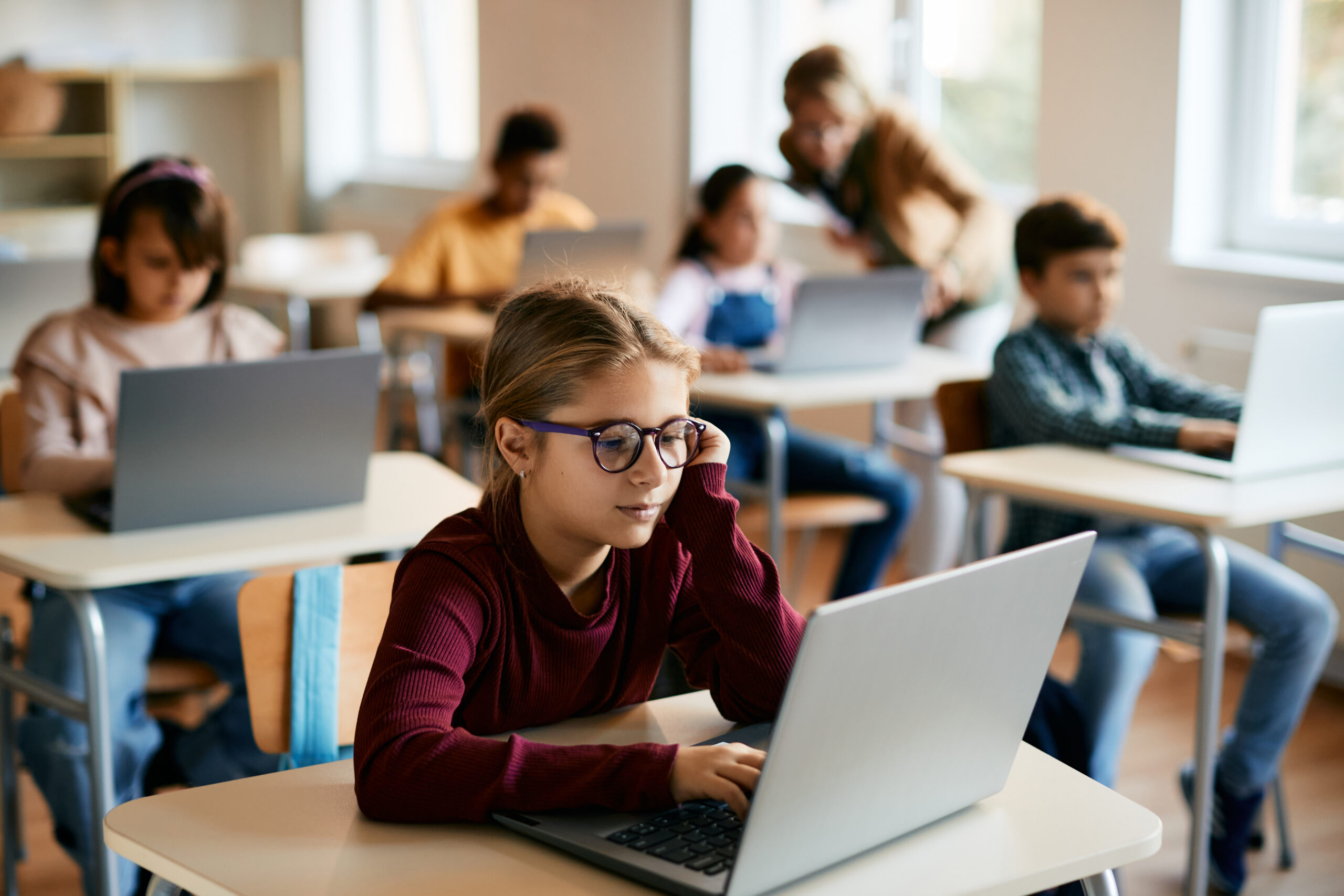 Little girl e-learns on laptop in computer science classroom at elementary school.